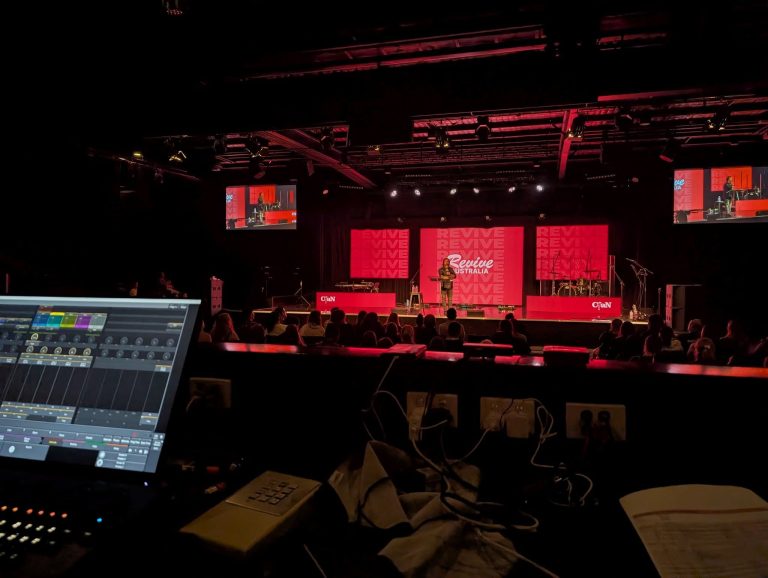 Conference stage lit in red with a digital mixing console at front of house