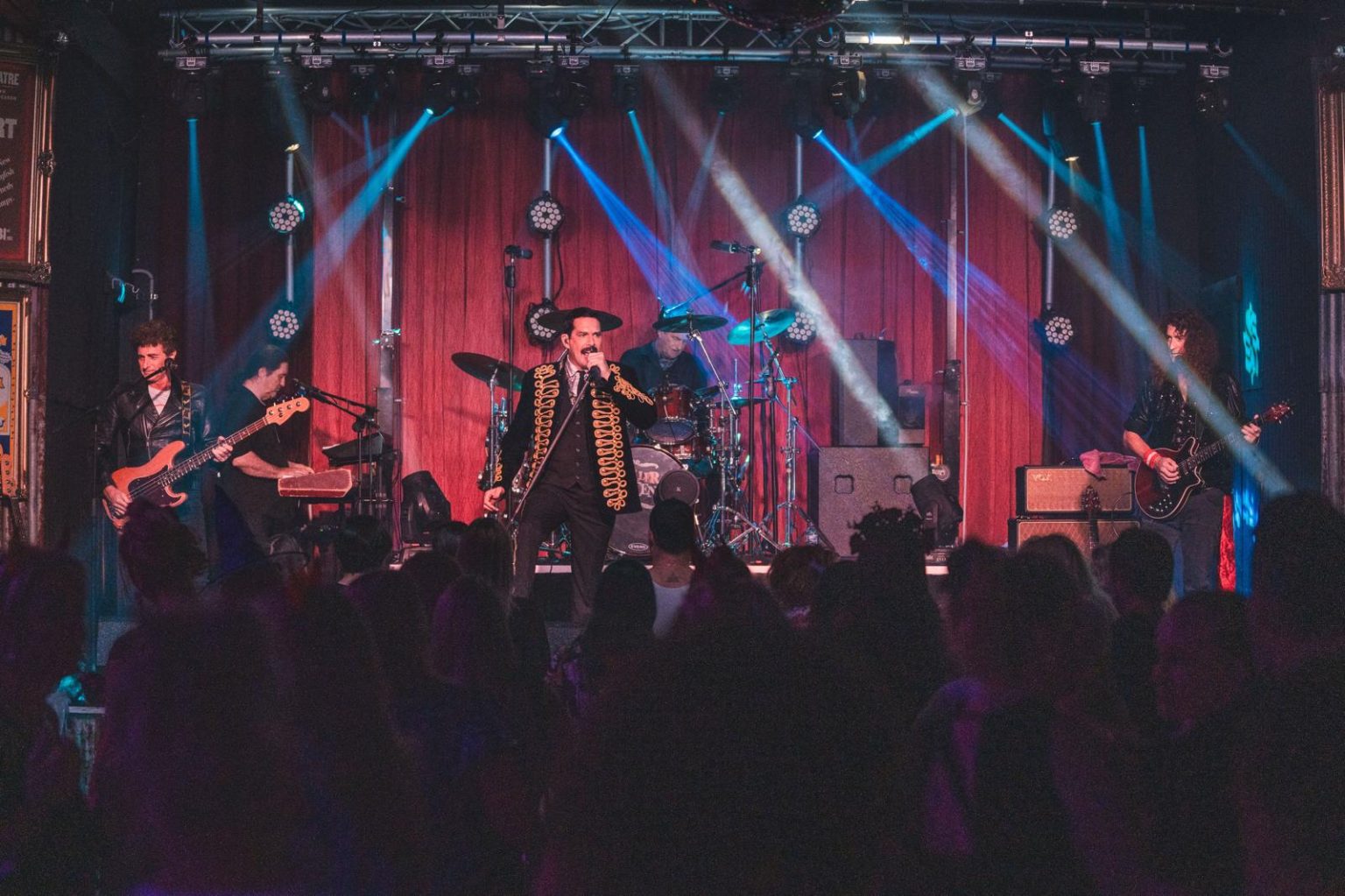 Live band on a lit stage with moving-head beams over a full audience