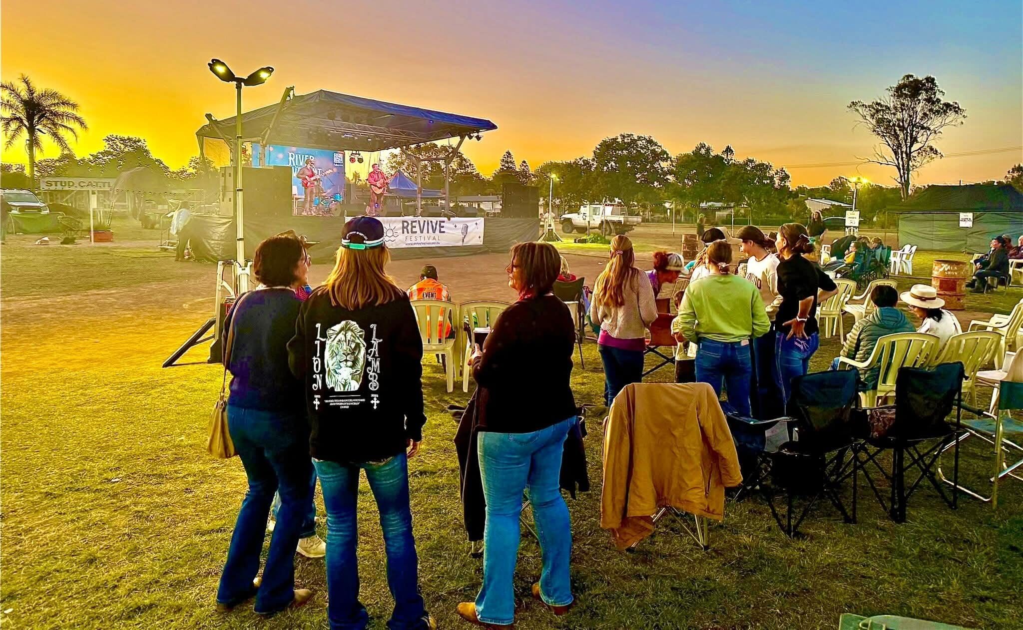 Crowd at the RAW Revive Festival in Mundubbera at sunset, watching a band on a covered trailer stage