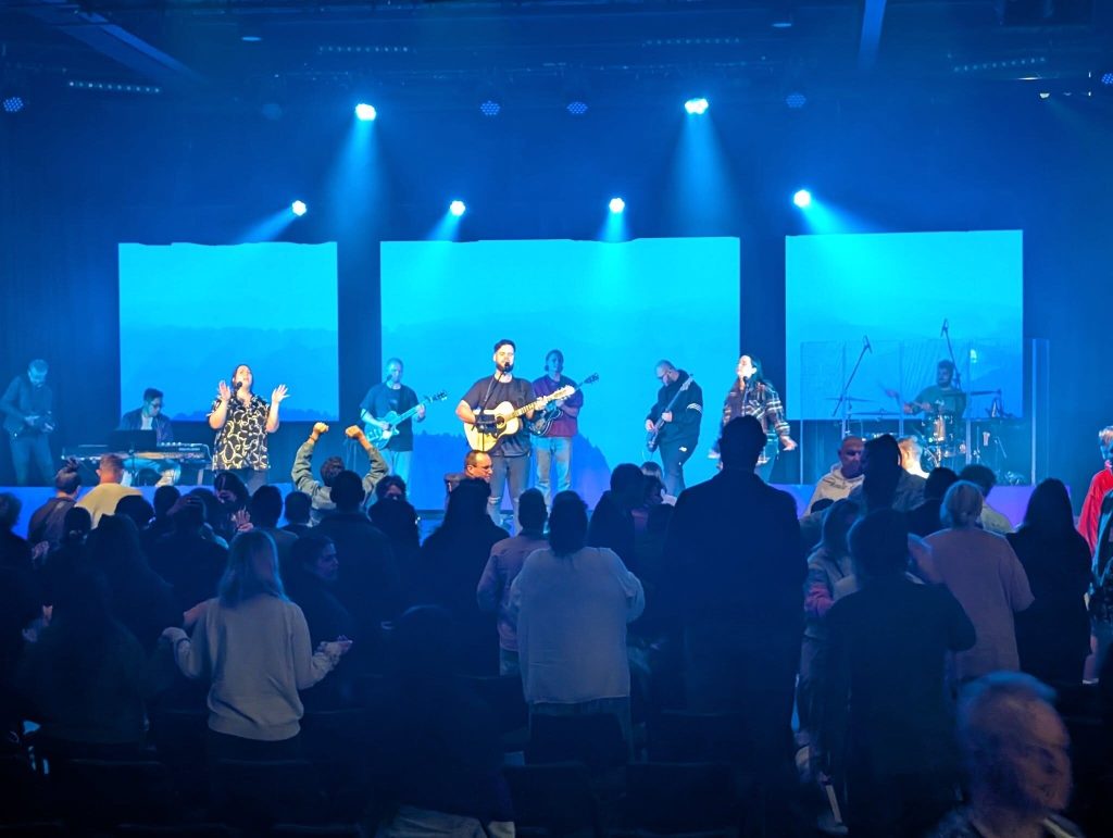 Congregation standing during a worship night, stage and screens washed in blue light